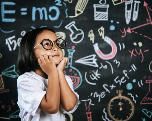 Portrait of happy little schoolchild wearing eyeglasses on background of backboard in school, smile and looking to camera in funny gesture